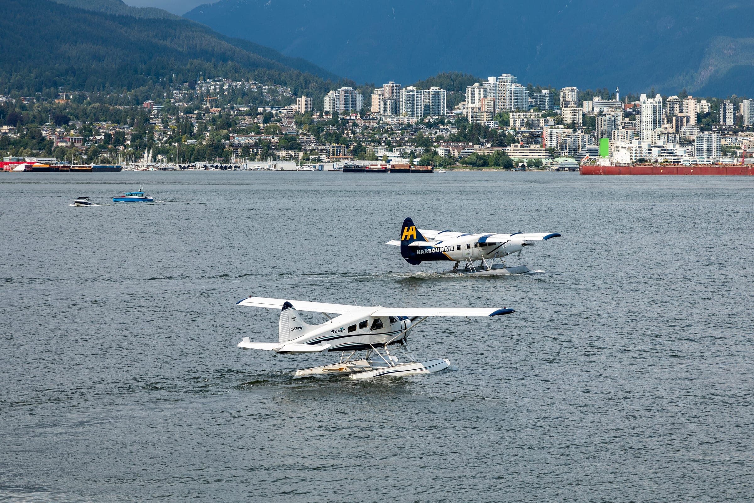 A Harbour Air seaplane lands on Burrard Inlet with the North Shore shoreline behind.