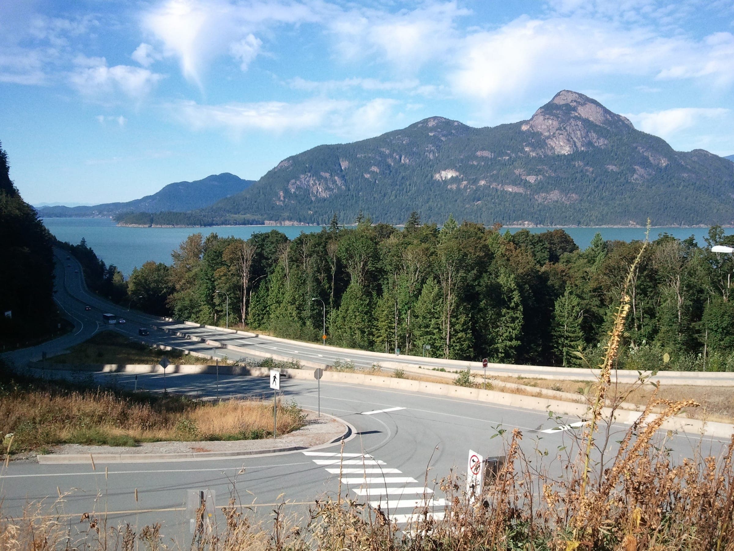 The Sea to Sky Highway curves above Howe Sound at Porteau Road with Mount Harvey beyond the water.
